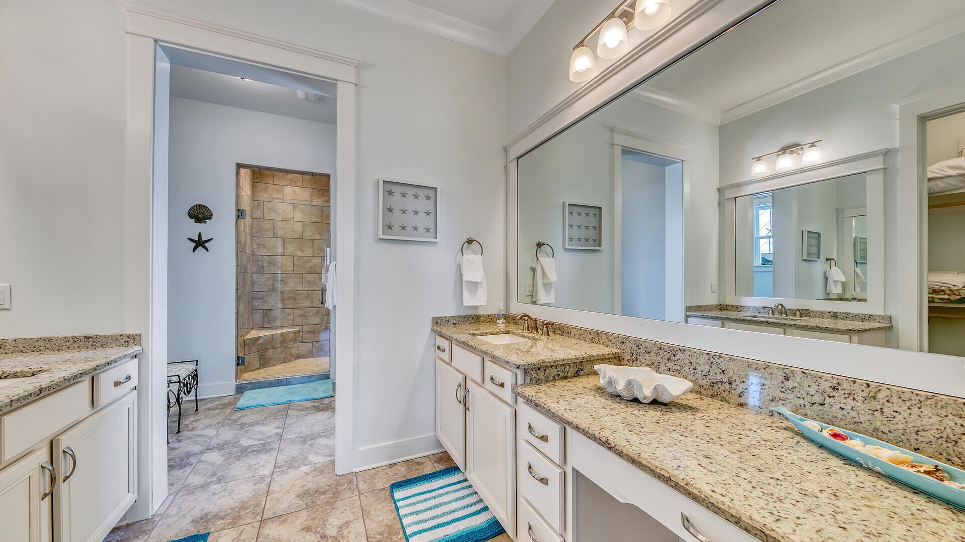 A bathroom with a large mirror, granite countertops, a shower, and a vanity with drawers.