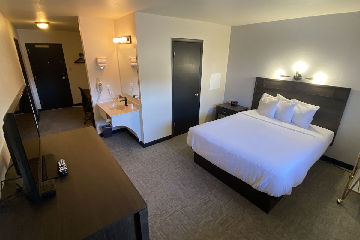 A hotel room with a bed, a desk, a chair, a mirror, a nightstand, and a TV.