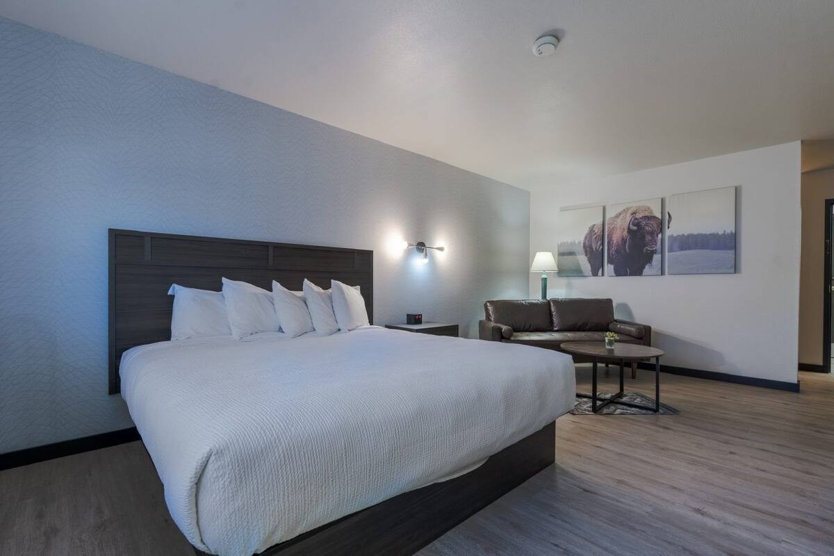 A modern hotel room with a large bed, a seating area with a sofa and armchairs, and a wall-mounted lamp.