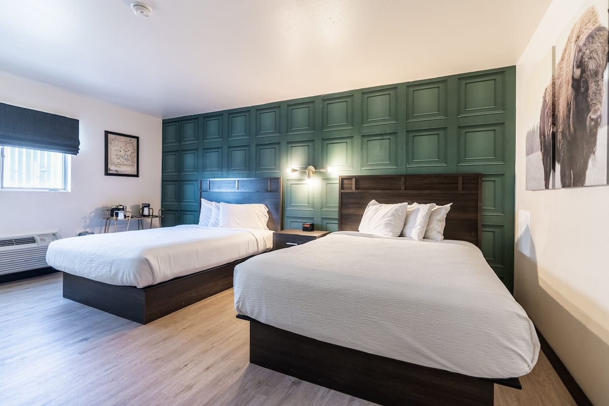A hotel room with two beds, a large window with a view, and a green accent wall.