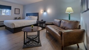 A hotel room with a bed, a sofa, a small table, and a lamp. - The Scout INN (Cody)