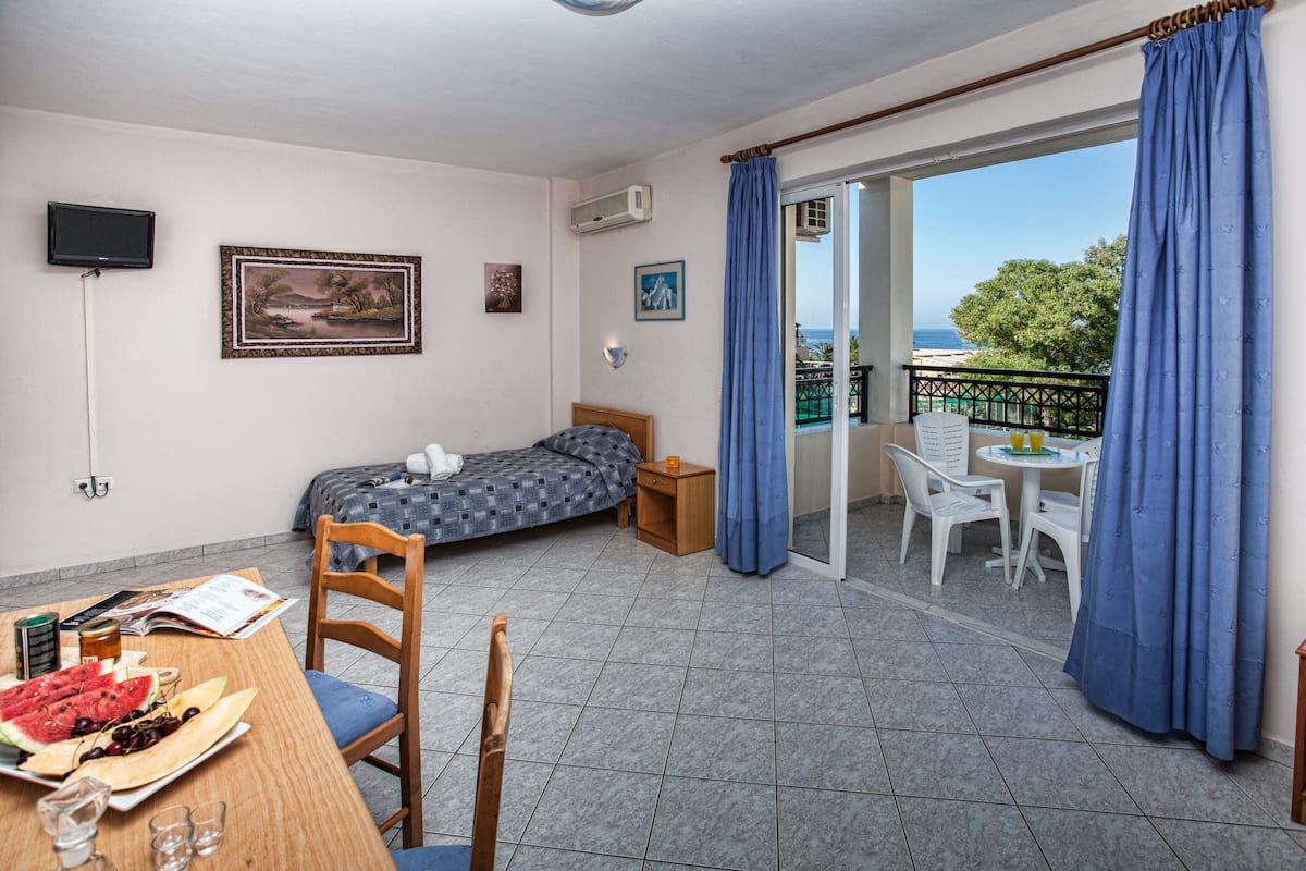 A room with a bed, a dining table with food, a TV, and a balcony with a view.