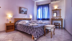 A bedroom with a bed, bedside tables, a nightstand, a small table with a chair, a mirror, and a window with curtains. - Bali Dorian Apartments (Mylopotamos)