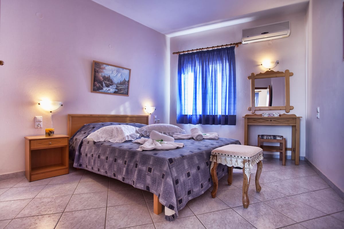 A bedroom with a bed, bedside tables, a nightstand, a small table with a chair, a mirror, and a window with curtains.