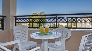 A balcony with white plastic chairs and a table, two glasses of orange juice, and a view of buildings and trees. - Bali Dorian Apartments (Mylopotamos)