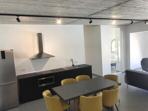 Une cuisine moderne dotée d’un îlot central, de meubles de rangement noirs et d’une hotte en acier inoxydable. On y trouve également un coin repas avec une table noire et des chaises jaunes.