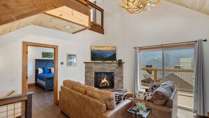 A spacious living room with a fireplace, a large sofa, a smaller sofa, and a dining area. - Modern 3 Bedroom Cabin with Mountain Views! (Sevierville)
