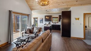 A spacious living room with a leather sofa, a dining area, and a kitchen with dark cabinets and a wooden ceiling. - Modern 3 Bedroom Cabin with Mountain Views! (Sevierville)