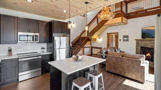 A modern kitchen with stainless steel appliances, a central island, and a staircase leading to a loft area. - Modern 3 Bedroom Cabin with Mountain Views! (Sevierville)
