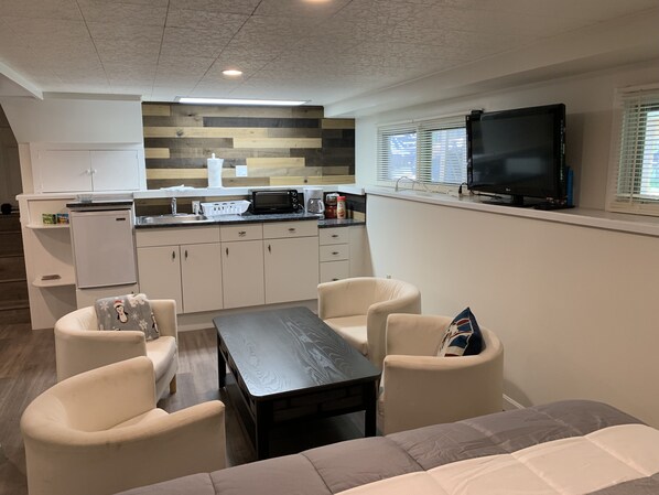 Cozy living space with a flat-screen TV, dining table, and sofa, plus a kitchenette with a refrigerator, microwave, and coffee maker.