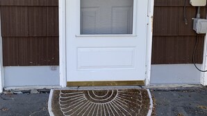 En vit ytterdörr med ett glasparti, en dörrmatta och ett eluttag på fasaden.