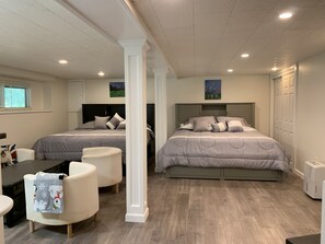 Two beds with grey duvets and pillows, a wooden floor, and a white column in a well-appointed bedroom.