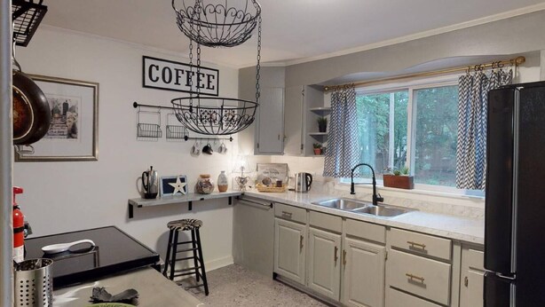 Una cocina con un cartel de café, una lámpara colgante, una ventana con cortinas y un refrigerador.