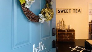 Una puerta azul con un letrero que dice 'hello' y una guirnalda. Se ve un letrero en la pared que dice 'SWEET TEA'.