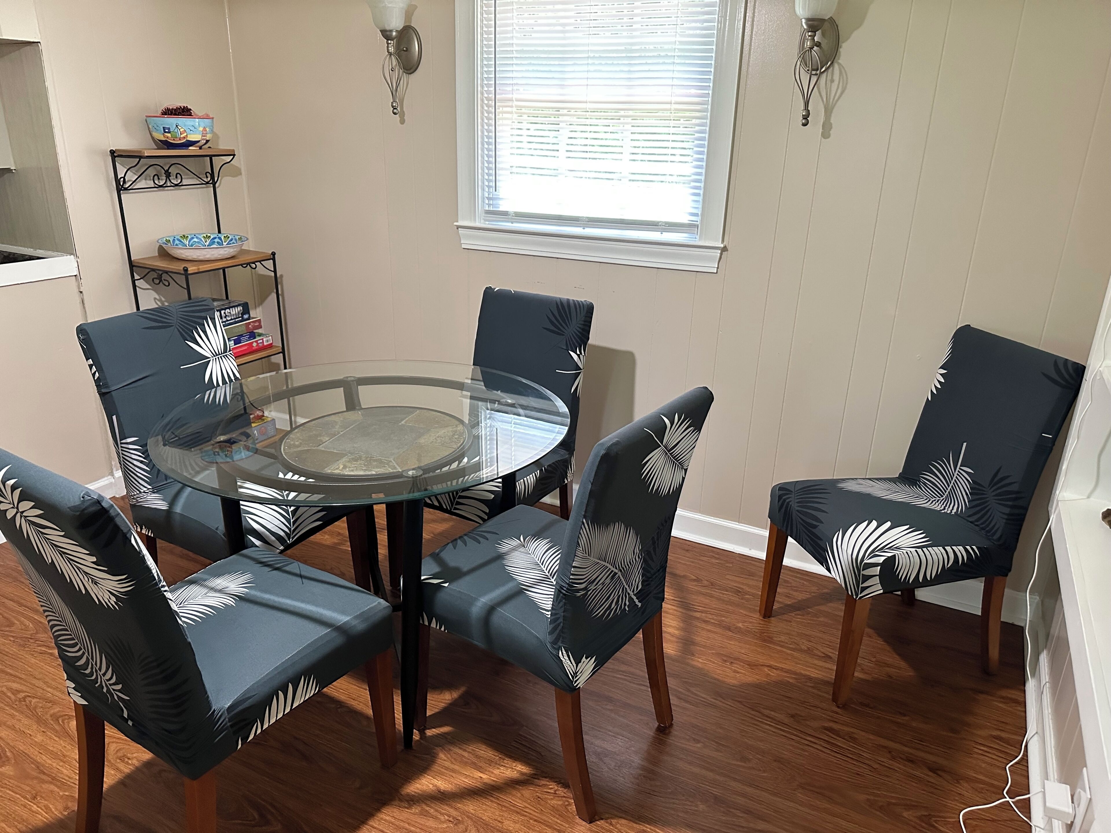 A dining area with a glass-top table surrounded by four chairs with leaf-patterned upholstery.