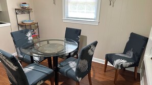 Comedor con una mesa de vidrio rodeada por cuatro sillas con tapicería estampada de hojas.