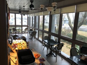 A covered outdoor dining area with wicker chairs and tables, large windows, and a decorative stained glass lamp.