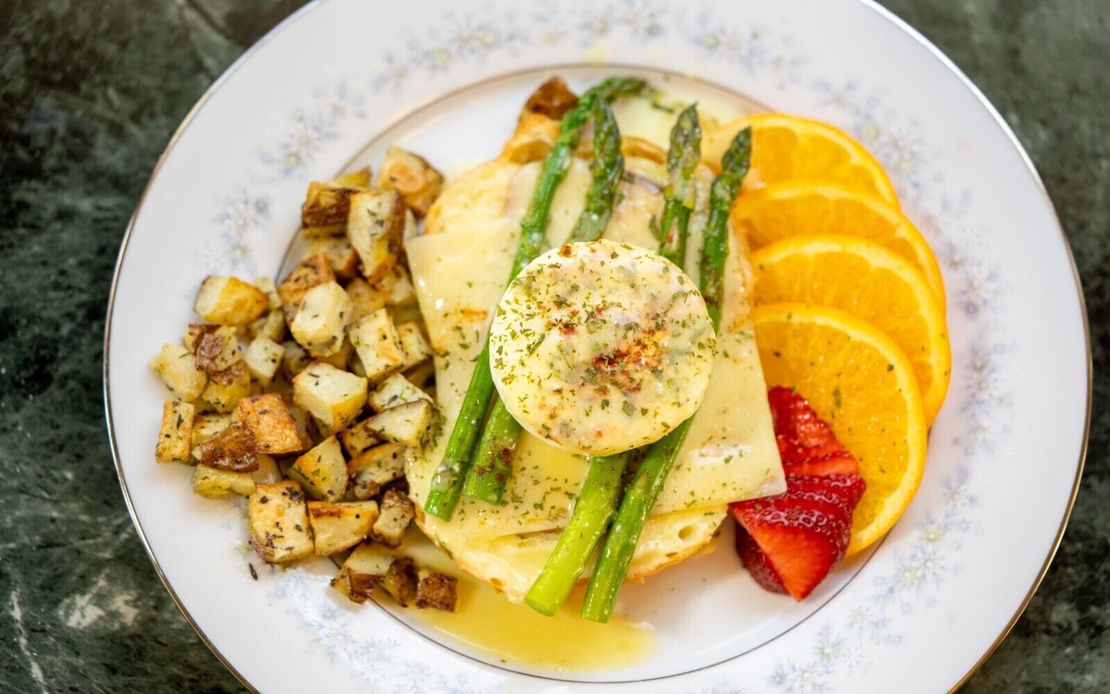 A plate of food with roasted potatoes, asparagus, orange slices, strawberries, and a poached egg.