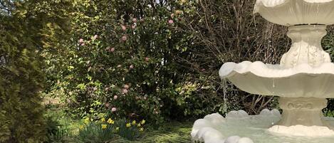 A tiered stone fountain surrounded by lush greenery and flowering bushes.