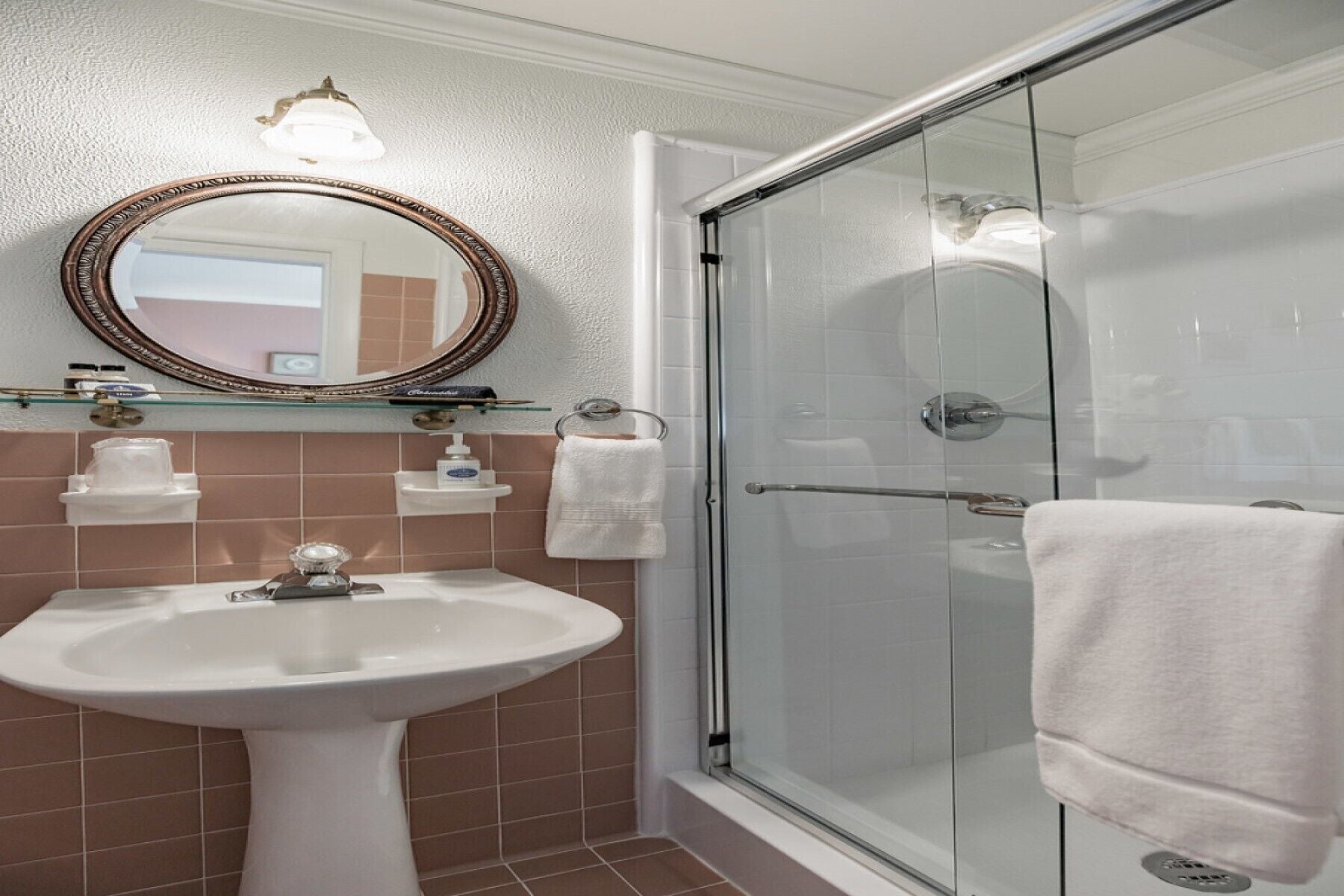 A bathroom with a white sink, a glass shower enclosure, and a mirror with a decorative frame.