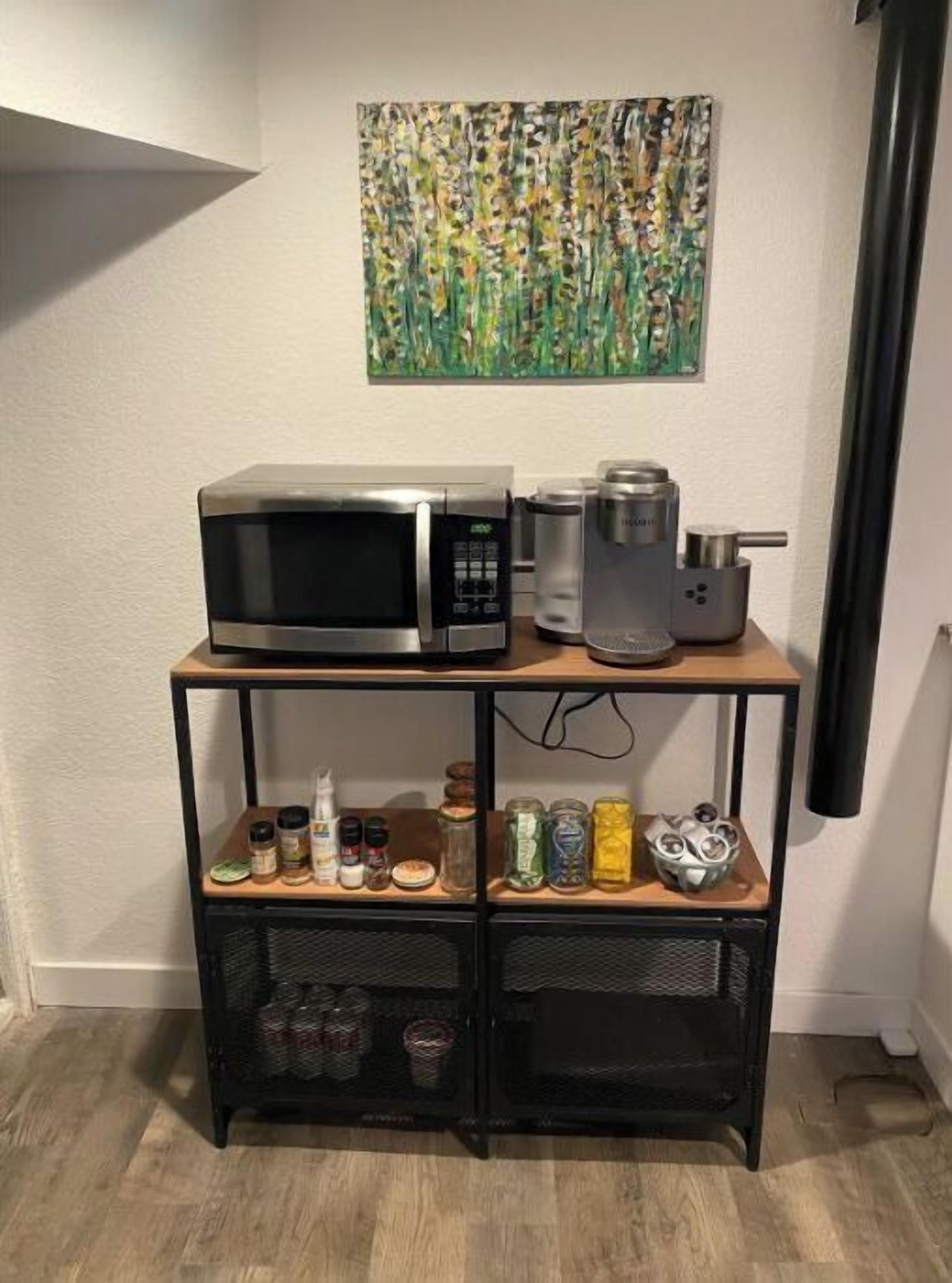 Un área de cocina con microondas, cafetera y diferentes especias en un estante.