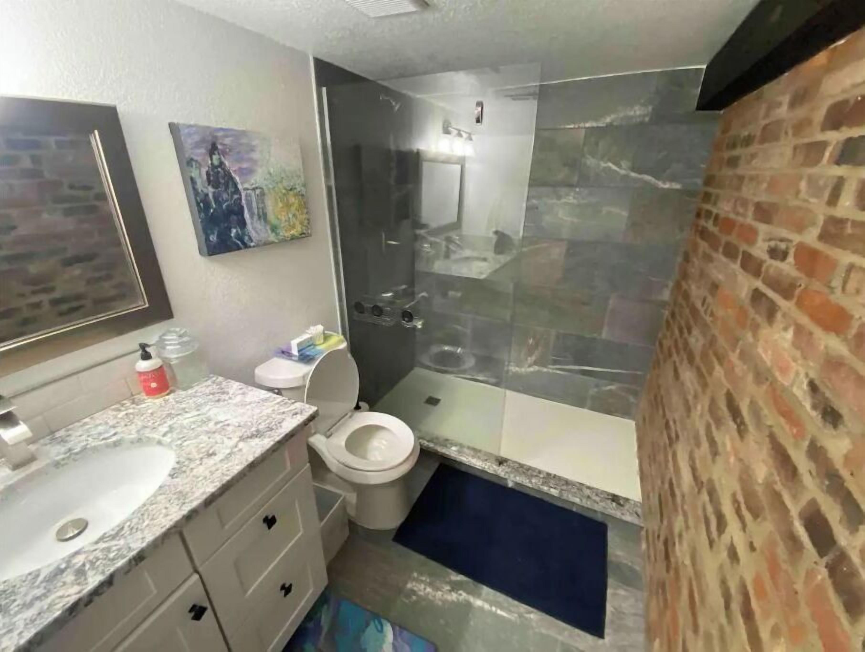 A bathroom with a marble sink, a toilet, a glass shower enclosure, and a brick wall.
