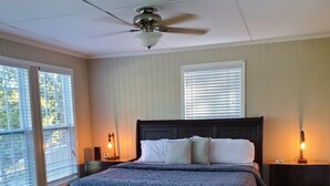A bedroom with a large bed, a ceiling fan, two bedside tables with lamps, and a window with blinds.