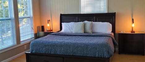 A bedroom with a large bed, a ceiling fan, two bedside tables with lamps, and a window with blinds.