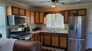 A kitchen with wooden cabinets, a stainless steel refrigerator, a microwave, a stove, and a ceiling fan.