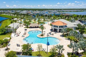 A resort with a large central pool, a beach area, and a view of the surrounding neighborhood.