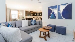 Una sala de estar moderna con un sofá gris, cojines azules y blancos, una mesa de centro de madera y un ventilador de techo.