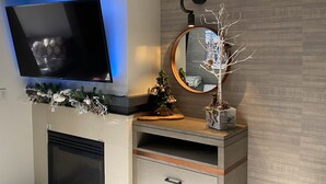 A modern living room with a flat-screen TV mounted on the wall, a fireplace, a decorative mirror, and a small Christmas tree. - Cozy & Pet friendly Studio at Monache Resort in Village (Mammoth Lakes)