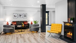 A modern living room with a sofa, two ottomans, a yellow armchair, a fireplace, and a coffee table with lamps. - Hotel One75 (Hamilton)