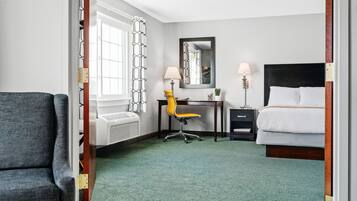 Een hotelkamer met een bed, een bureau met stoel, een spiegel en een raam met gordijnen.