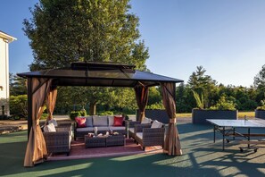 An outdoor seating area with a pergola, wicker furniture, and a ping pong table.