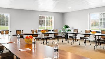 Una sala conferenze con un lungo tavolo, sedie, bottiglie d'acqua e una ciotola di frutta.
