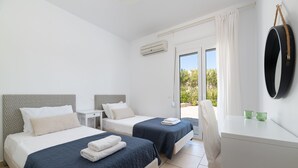 Habitación de hotel con dos camas, un escritorio y una silla. Tiene una ventana con cortinas, un aire acondicionado y vistas a zonas verdes.