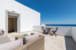 Ein Balkon mit Korbmöbeln, einem Tisch mit Flaschen und Blick aufs Meer.