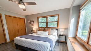 Une chambre avec un grand lit, un ventilateur de plafond, une fenêtre avec des stores et une armoire en bois.