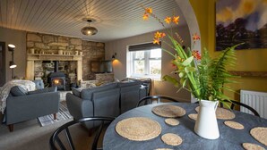 A cozy living room with a stone fireplace, grey sofas, and a round table with woven placemats. - Cosy, Tranquil, Fully Equipped & Beautiful Garden (Chathill)