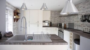 A modern kitchen with white cabinets, a stainless steel sink, and pendant lighting. - Cosy, Tranquil, Fully Equipped & Beautiful Garden (Chathill)