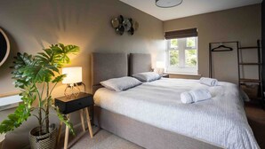 A bedroom with a bed, bedside table, lamp, potted plant, and a window with a view. - Cosy, Tranquil, Fully Equipped & Beautiful Garden (Chathill)