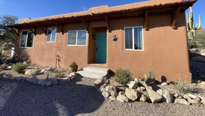 A stucco house with a flat roof, a front door, and three windows.