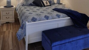 A bedroom with a bed, two bedside lamps, a ceiling fan, and two framed pictures on the wall.