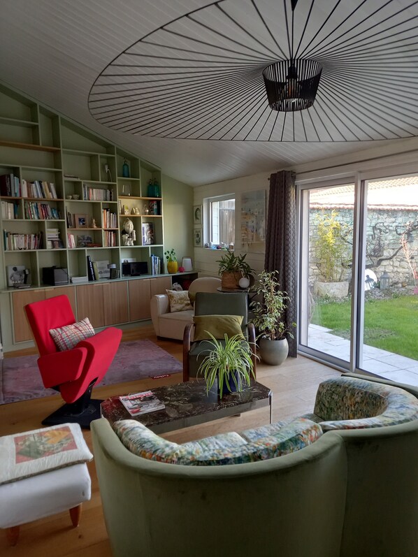 Un salon comprenant un canapé, des fauteuils, une table basse, une bibliothèque et une grande fenêtre donnant sur l’extérieur.