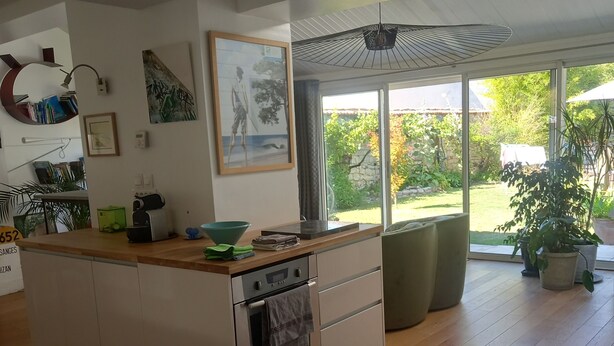 A modern kitchen with a central island, built-in oven, and large windows offering a view of the garden. - House (AYTRE)