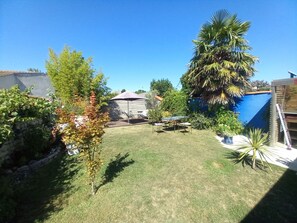 Un jardin avec une table et des chaises de patio, entouré de différentes plantes et d’un grand arbre.