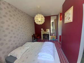 Une chambre d’hôtel avec un lit, un miroir, une cheminée et un tableau au mur.