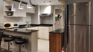 A modern kitchen with a stainless steel refrigerator, two pendant lights, a microwave, and a bar area with stools.