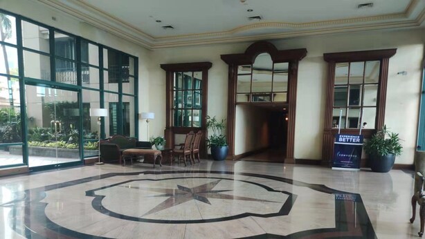 A spacious lobby with a large circular floor design, a reception desk, and several potted plants.